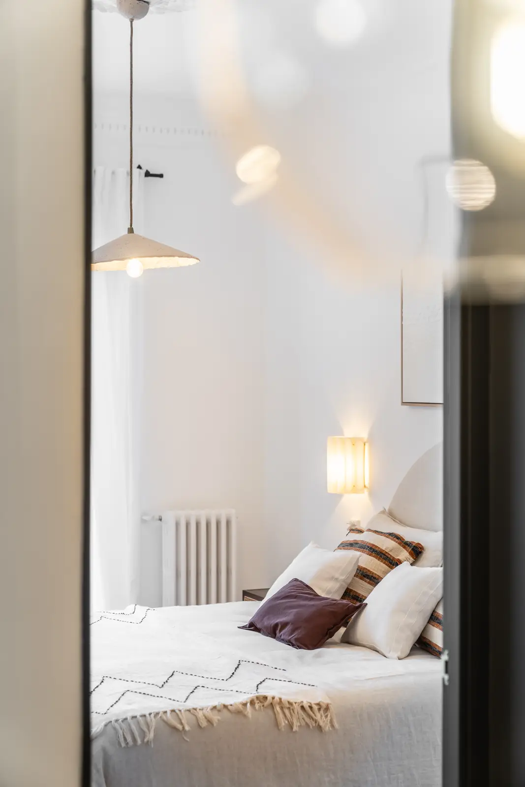 Dormitorio luminoso con cama vestida, cojines y lámpara colgante