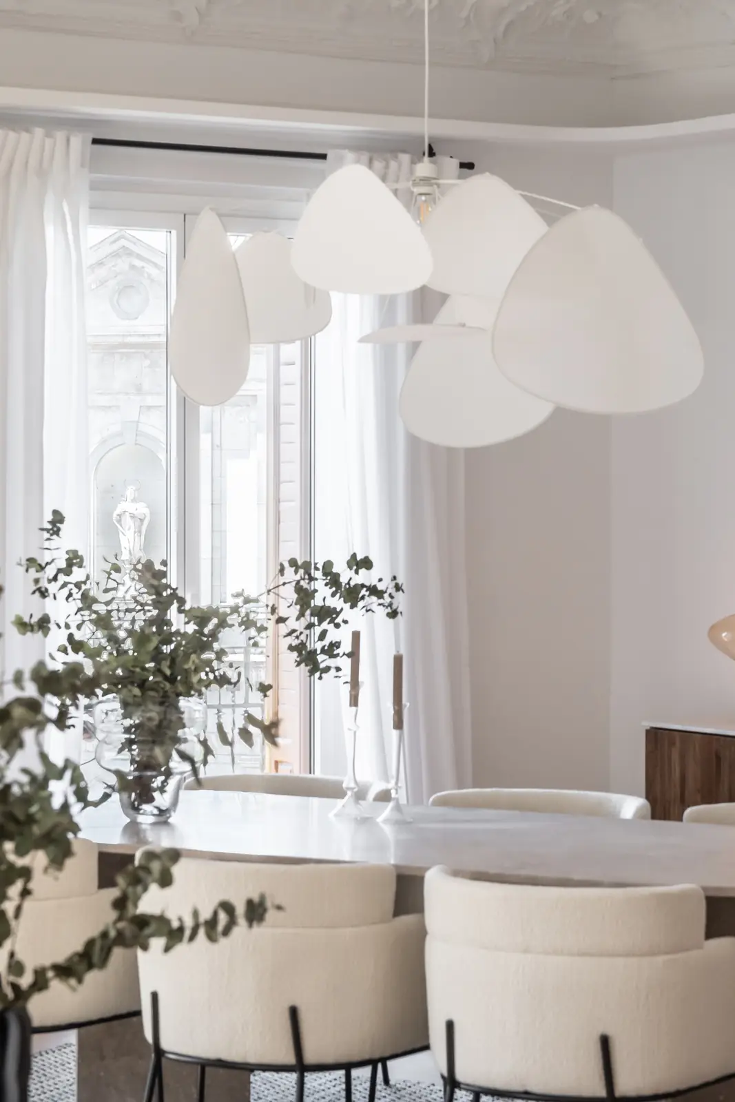 Zona de comedor junto a ventanal con mesa redonda, sillas beige y lámpara de diseño