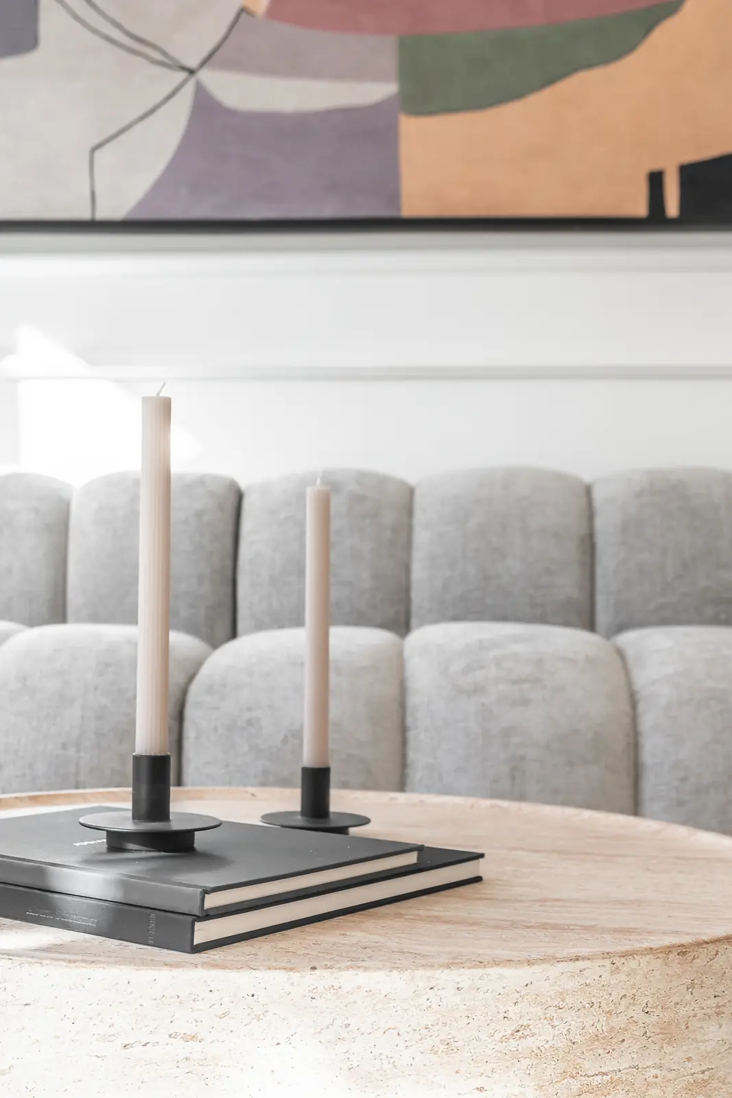 Detalle decorativo con velas y sofá gris capitoné sobre mesa de travertino